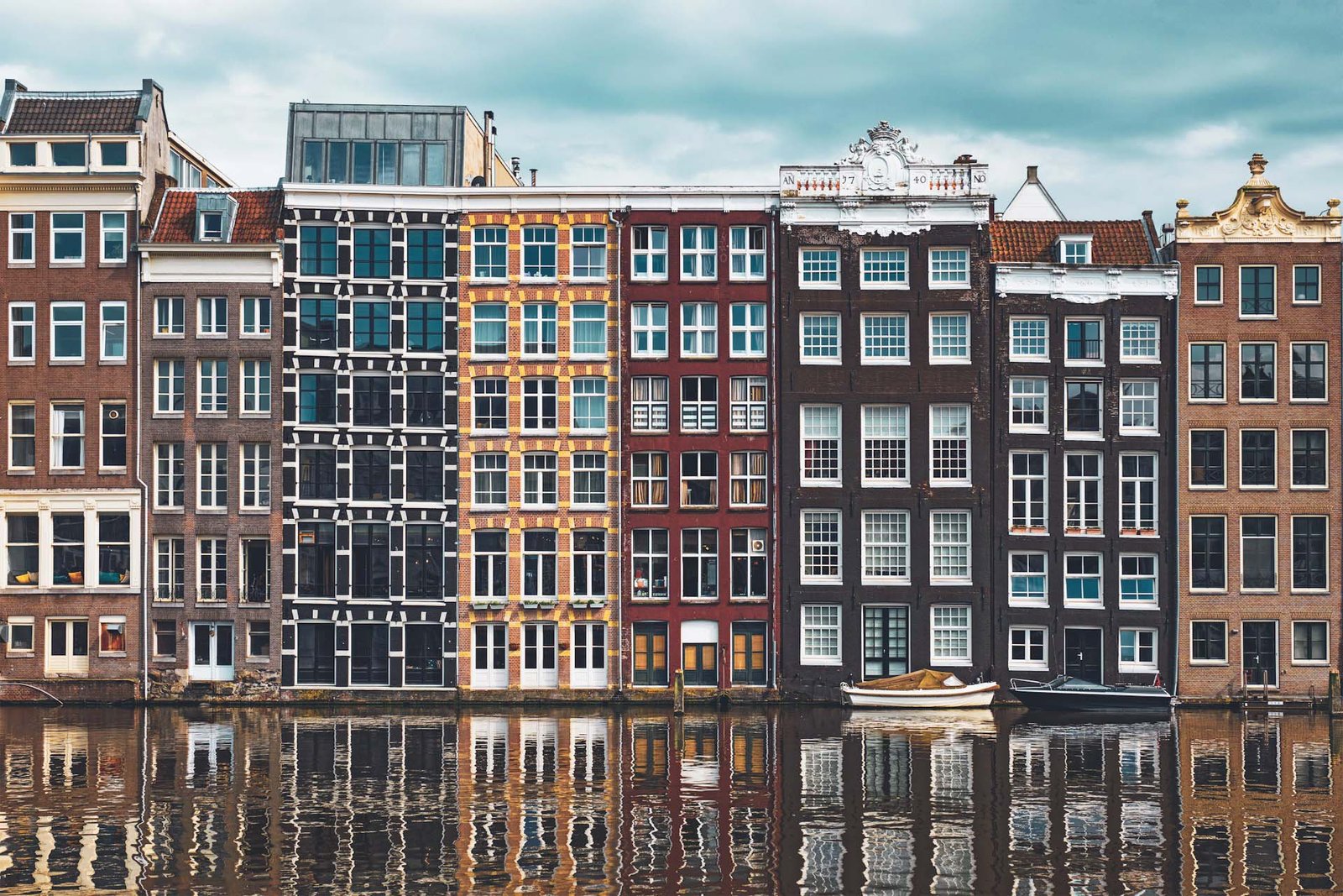 Row-of-typical-houses-and-boat-on-amsterdam-canal-damrak-with-reflection-amsterdam-netherlands
